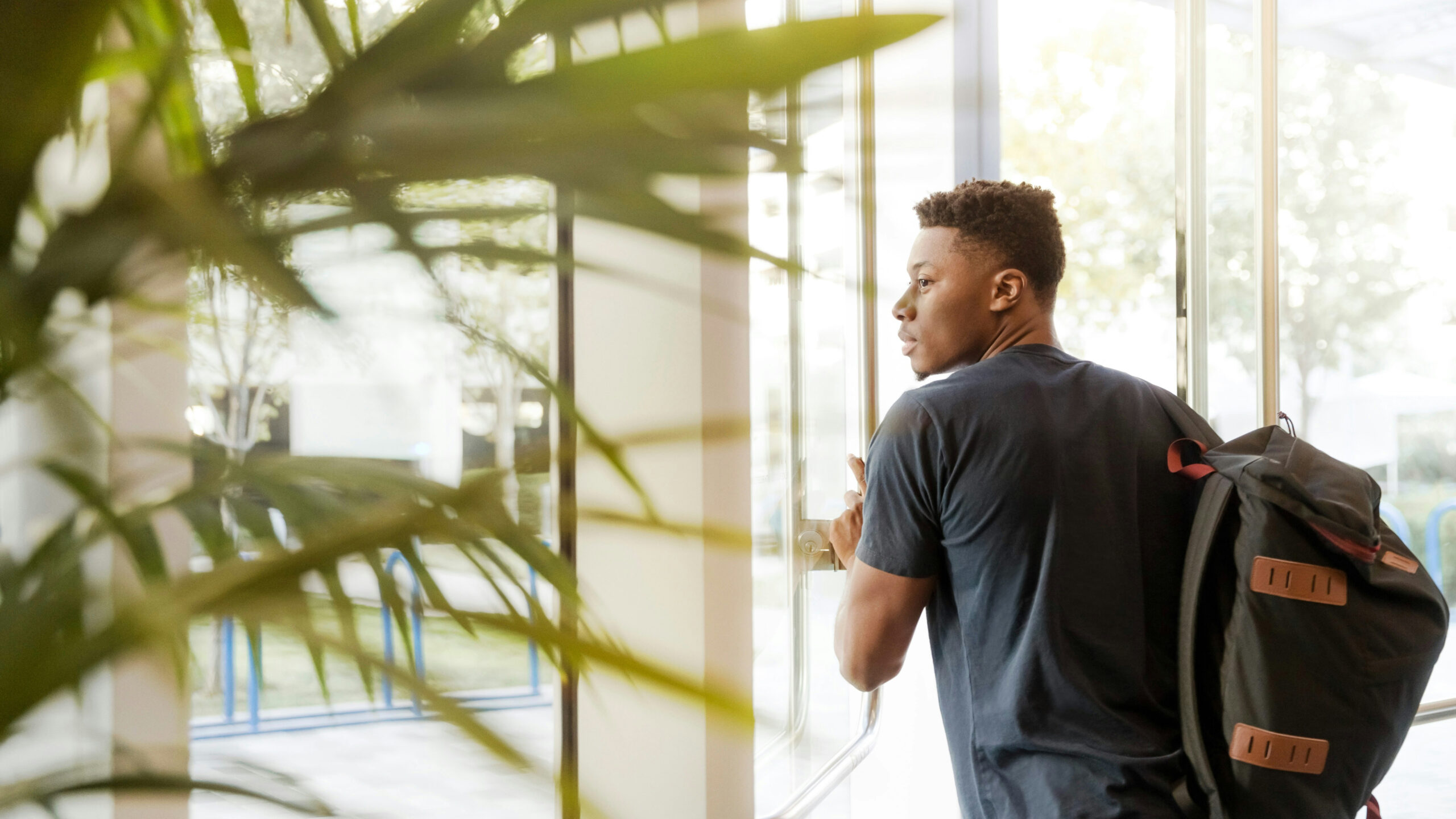 A young man with a backpack walking out of a building.
